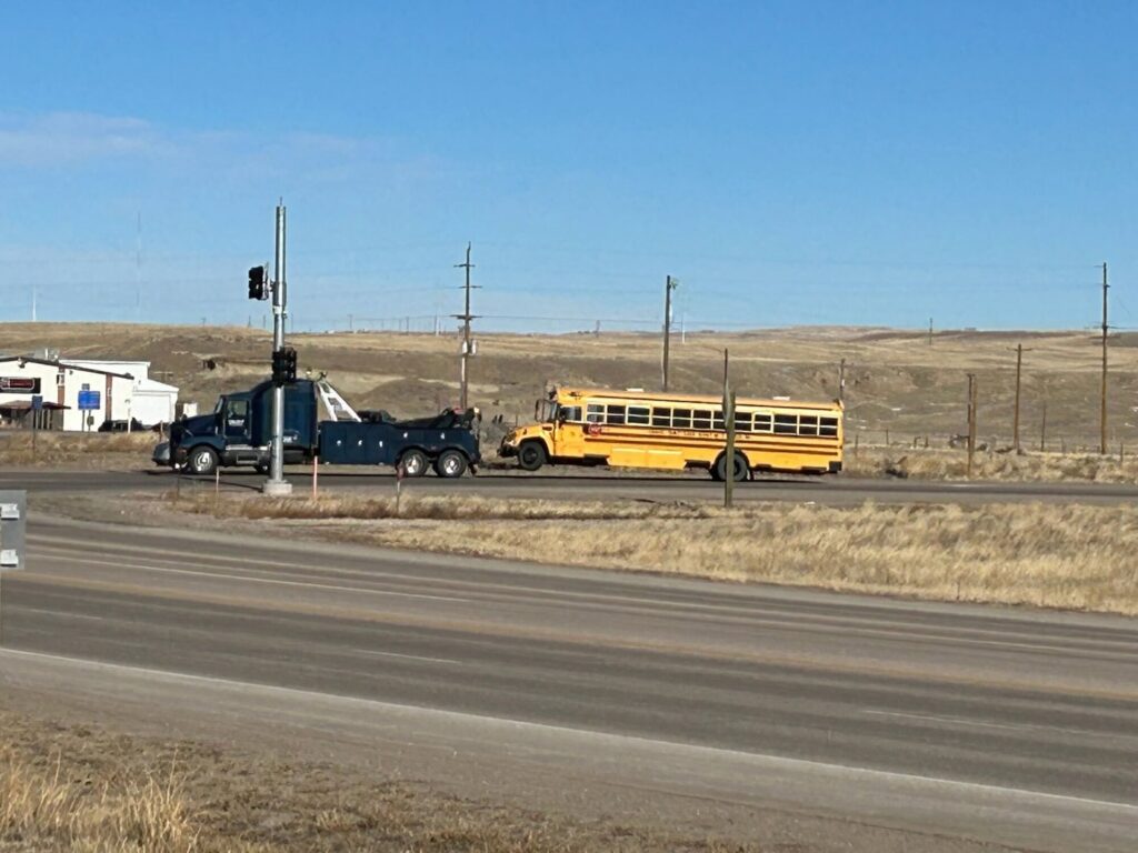 A heavy-duty tow truck from Select Towing and Recovery towing a yellow school bus on a clear day in Casper, WY.