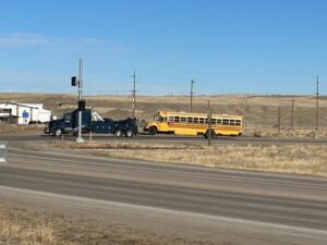 A heavy-duty tow truck from Select Towing and Recovery towing a yellow school bus on a clear day in Casper, WY.