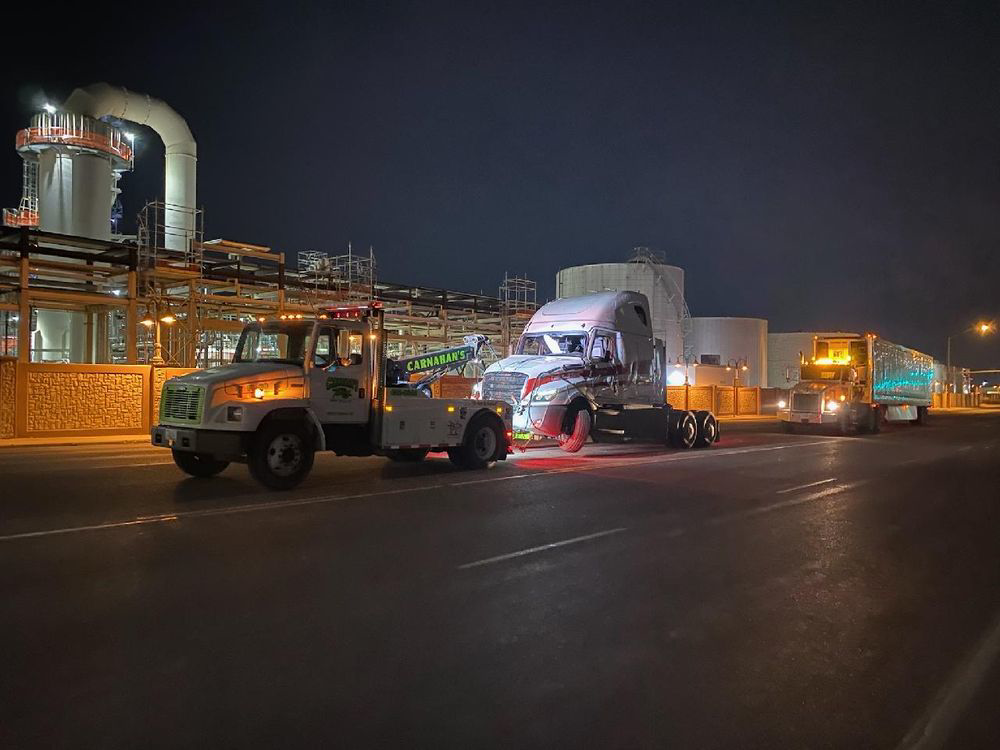 A heavy-duty tow truck from Carnahan's Towing & Repair Inc. towing a semi-truck cab at night in Great Falls, MT.