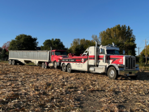A heavy-duty tow truck from MAD J Repair & Towing actively towing a semi-truck with a trailer in a field in Des Moines, IA.
