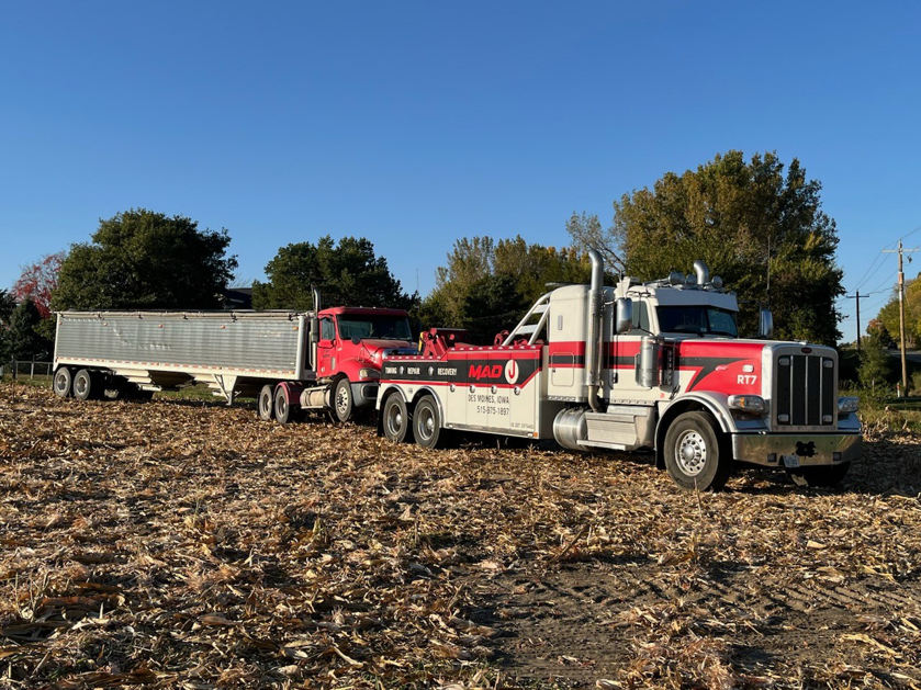 A heavy-duty tow truck from MAD J Repair & Towing actively towing a semi-truck with a trailer in a field in Des Moines, IA.
