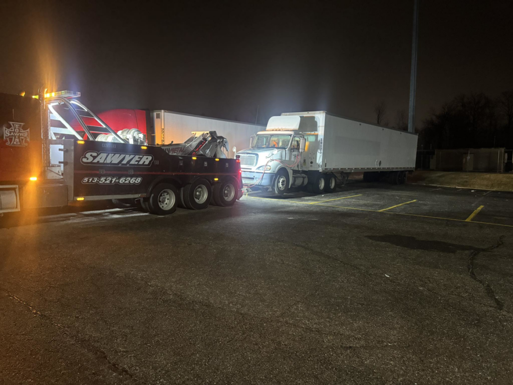 A heavy-duty tow truck from Sawyer Towing is actively towing a semi-truck at night in Cincinnati, OH.