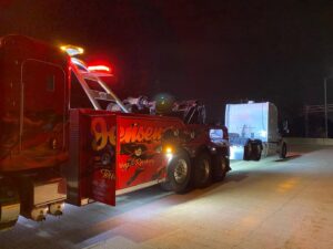 A heavy-duty tow truck from Jensen Towing towing a semi-truck trailer at night in Kenosha, WI.