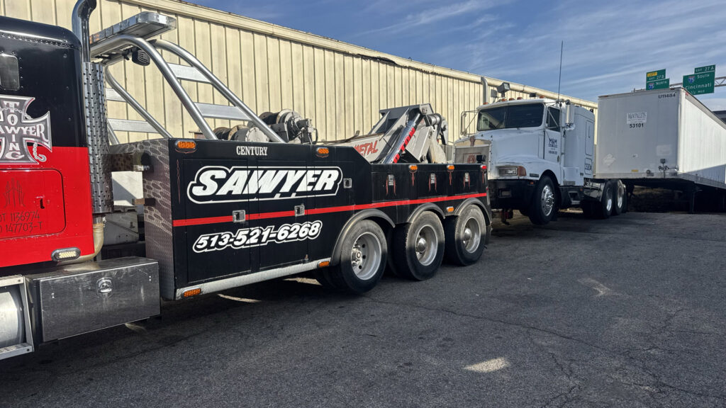 A heavy-duty tow truck from Sawyer Towing is actively towing a semi-truck trailer in Cincinnati, OH.