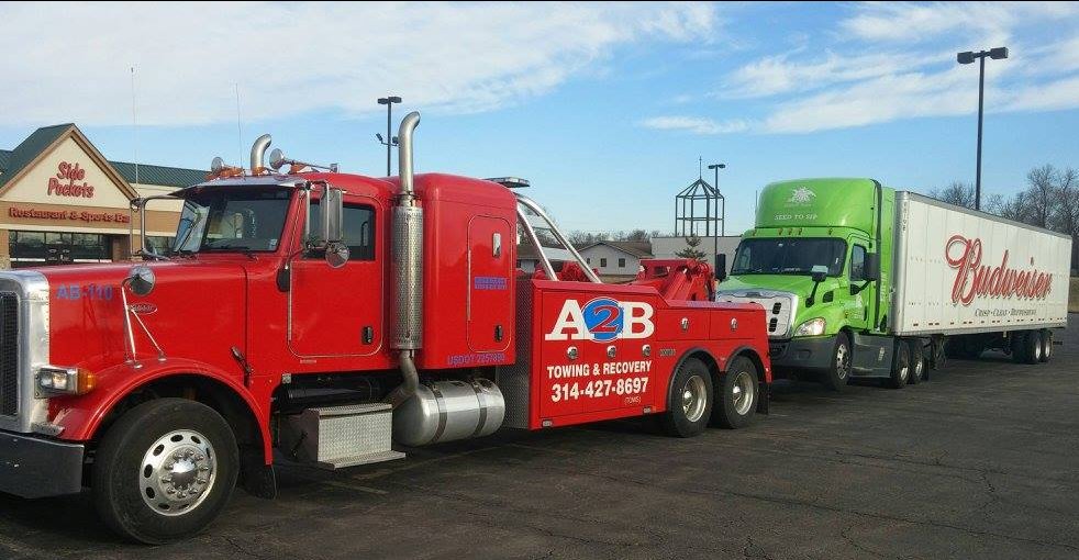 A heavy-duty tow truck from A2B Towing & Recovery towing a green semi-truck in Hazelwood, MO.