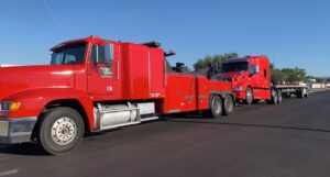 A red heavy-duty tow truck from Power Towing & Transport towing a red semi-truck cab and trailer in Phoenix, AZ.