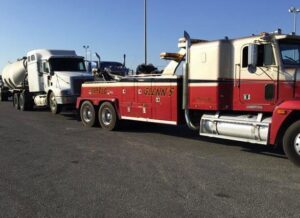 A red and white heavy-duty tow truck from Glenn's Towing & Recovery Inc towing a white tanker truck in Lafayette, LA.