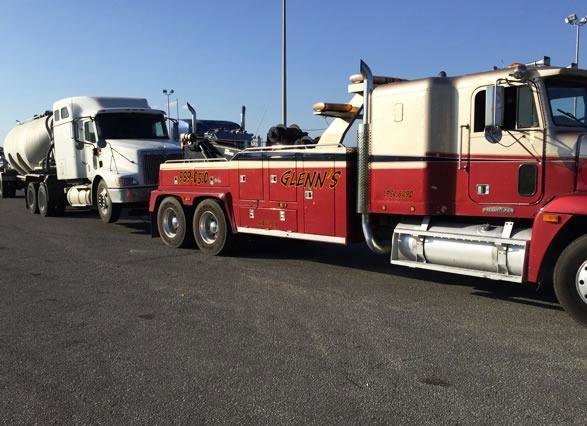 A red and white heavy-duty tow truck from Glenn's Towing & Recovery Inc towing a white tanker truck in Lafayette, LA.