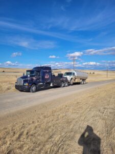 A heavy-duty tow truck from Select Towing and Recovery towing a tanker truck on a rural road in Casper, WY.