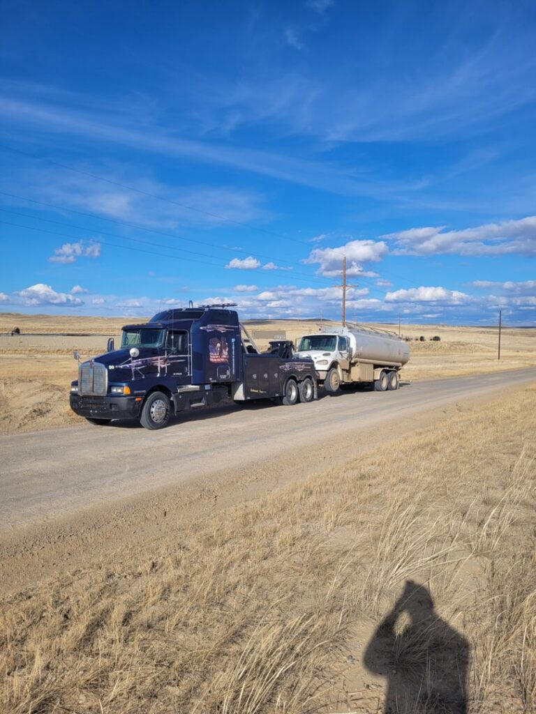 A heavy-duty tow truck from Select Towing and Recovery towing a tanker truck on a rural road in Casper, WY.