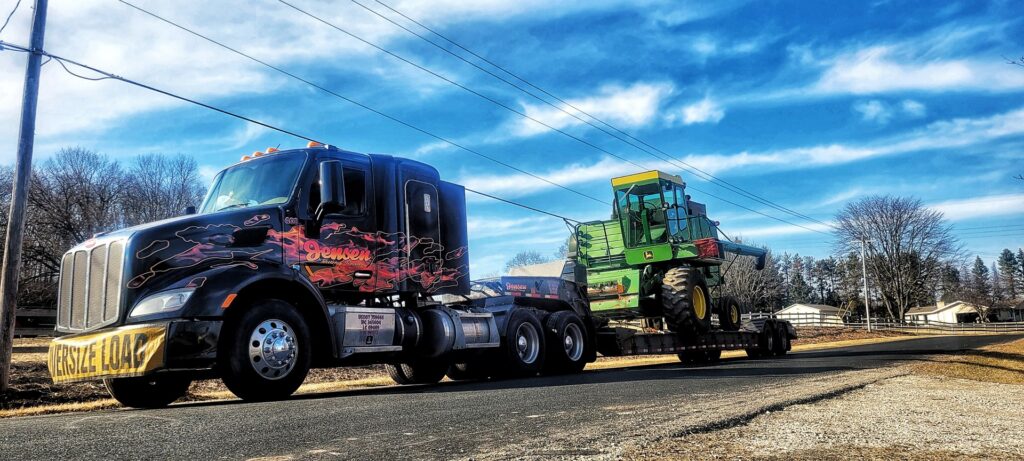 A heavy-duty tow truck from Jensen Towing transporting a large green combine harvester in Kenosha, WI.
