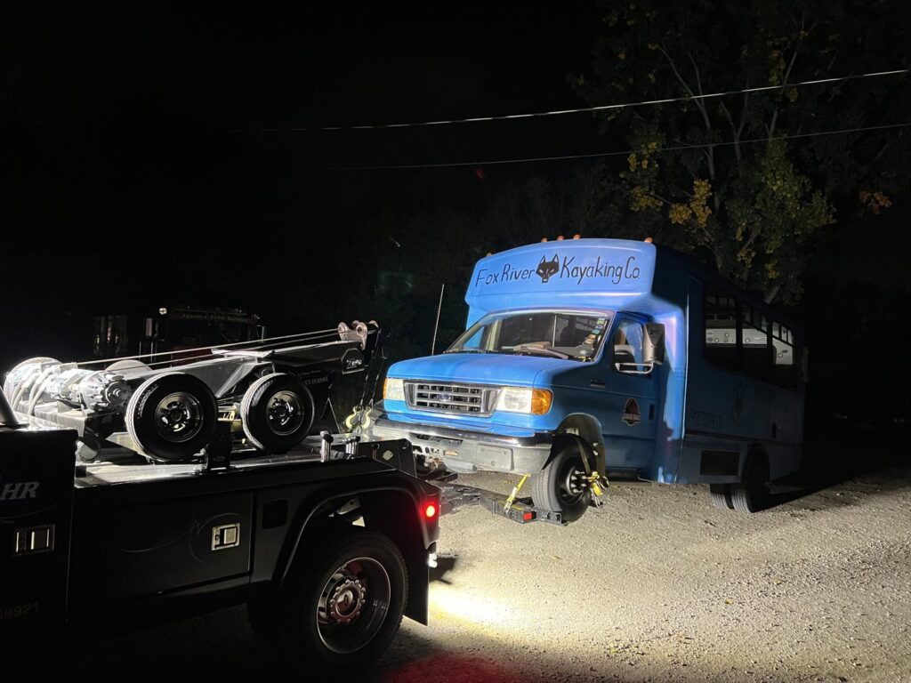A&W Towing and Repair heavy-duty tow truck preparing to tow a blue bus at night in Appleton, WI.