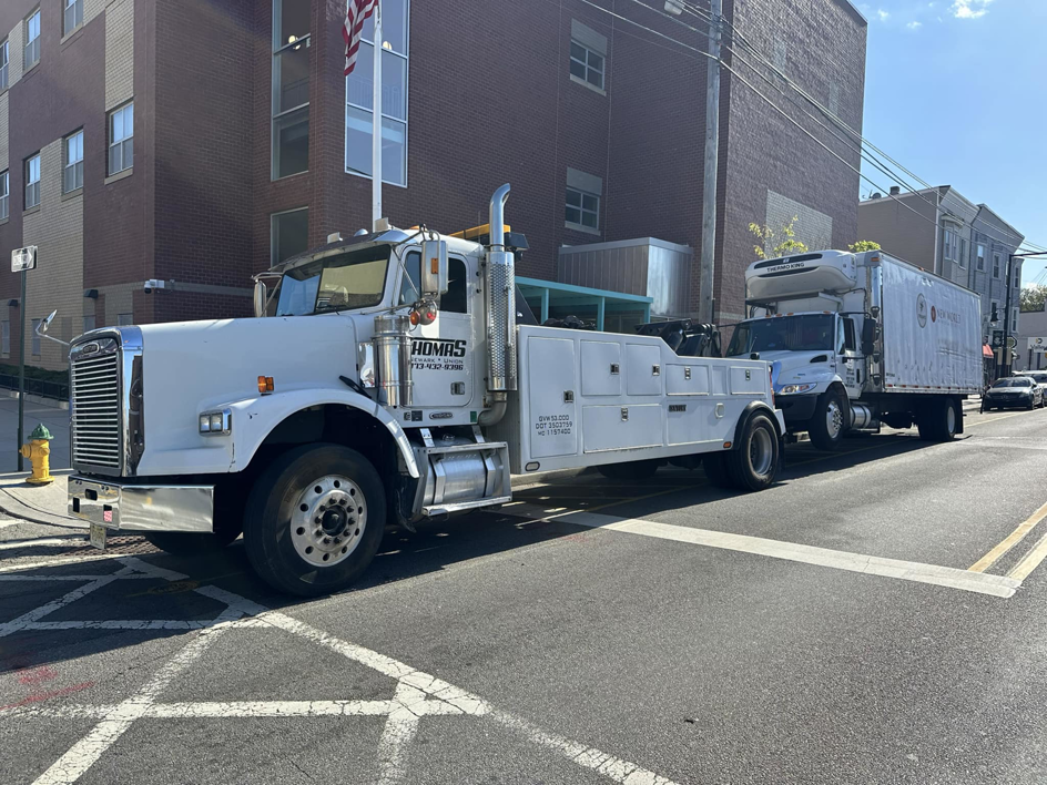Thomas Towing & Recovery heavy-duty truck towing a large white box truck in Newark, NJ.