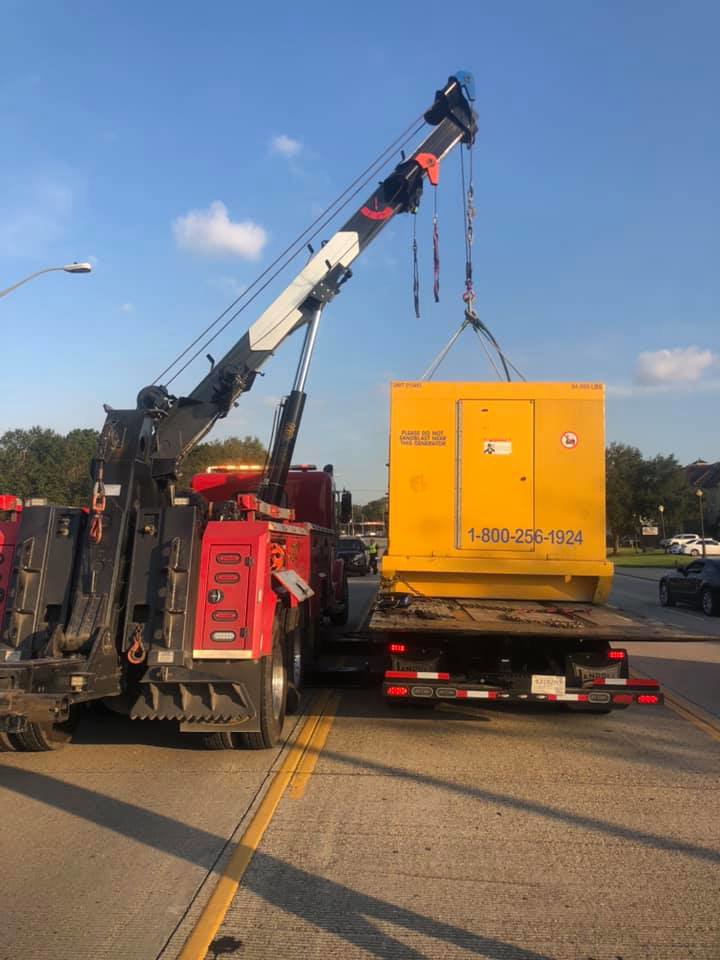 A heavy-duty wrecker from Glenn's Towing & Recovery Inc lifting a large yellow generator onto a trailer in Lafayette, LA.