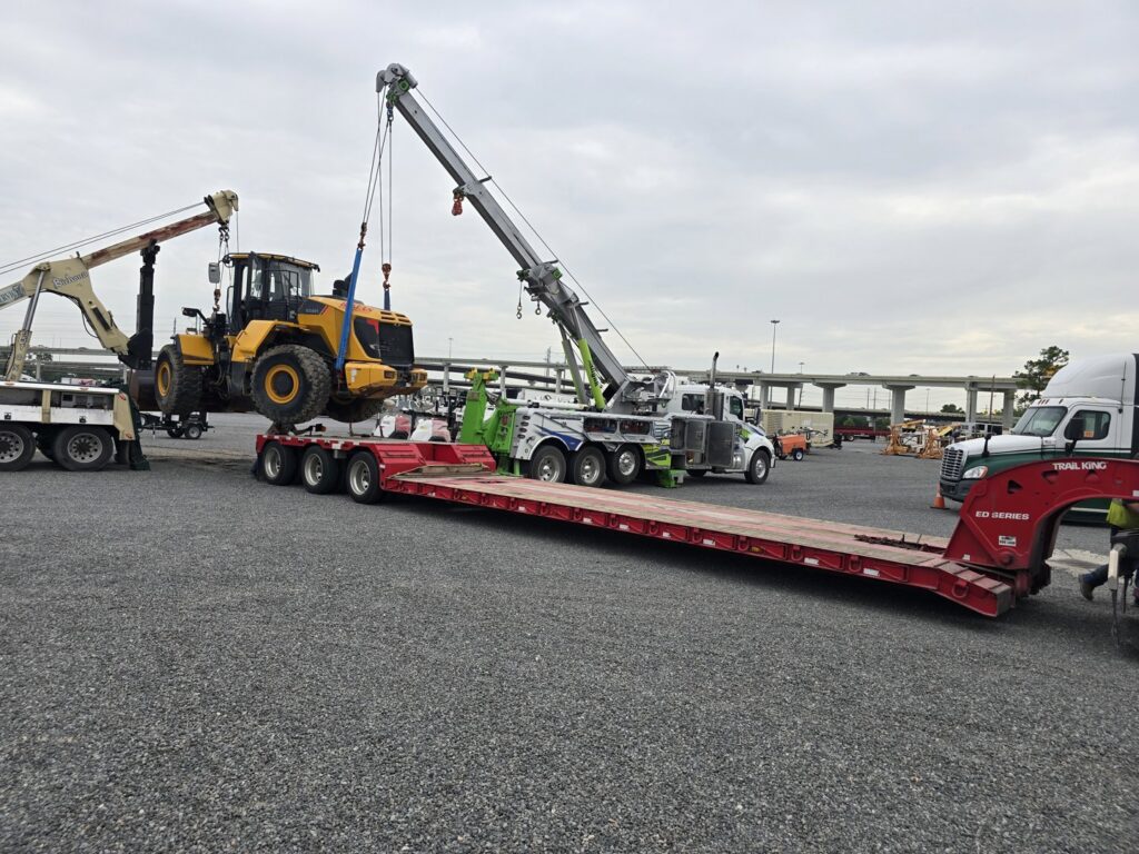 A heavy-duty wrecker from Allan Motors & Wrecker Service LLC lifting a large yellow loader onto a trailer in Houston, TX