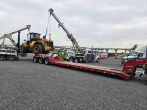A heavy-duty wrecker from Allan Motors & Wrecker Service LLC lifting a large yellow loader onto a trailer in Houston, TX