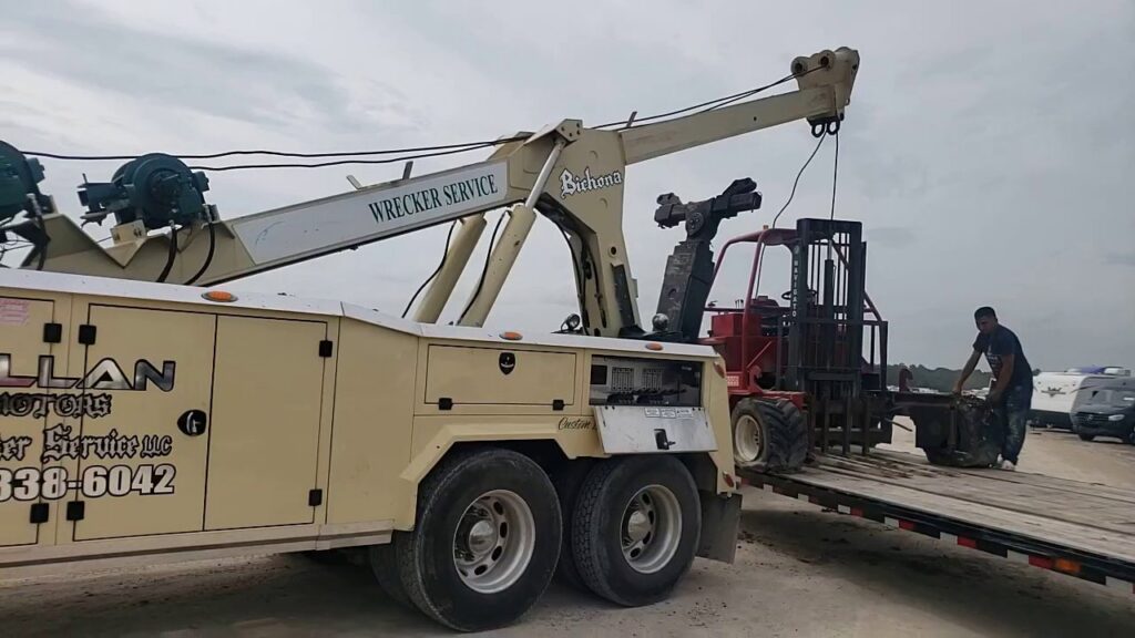 A heavy-duty wrecker from Allan Motors & Wrecker Service LLC loading a red forklift onto a trailer in Houston, TX