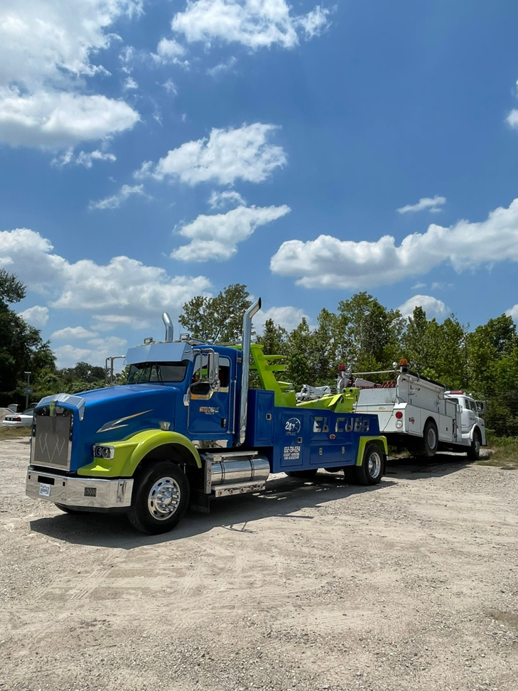 A heavy-duty wrecker from Santos Wrecker Services in Houston, TX, towing a white truck on a sunny day.