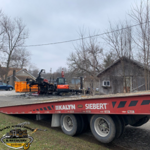Heavy equipment recovery of a burnt excavator and dumpster on a flatbed trailer by Sunny Acres Towing in Greenville, IN.