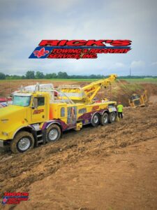 A heavy-duty wrecker from Rick's Towing and Recovery in Lafayette, LA, recovering heavy equipment from a muddy field.