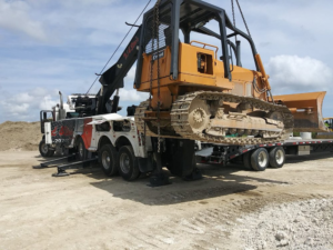 A heavy-duty tow truck from Ted & Stan's Towing Service lifting a bulldozer onto a flatbed trailer in Cutler Bay, FL.
