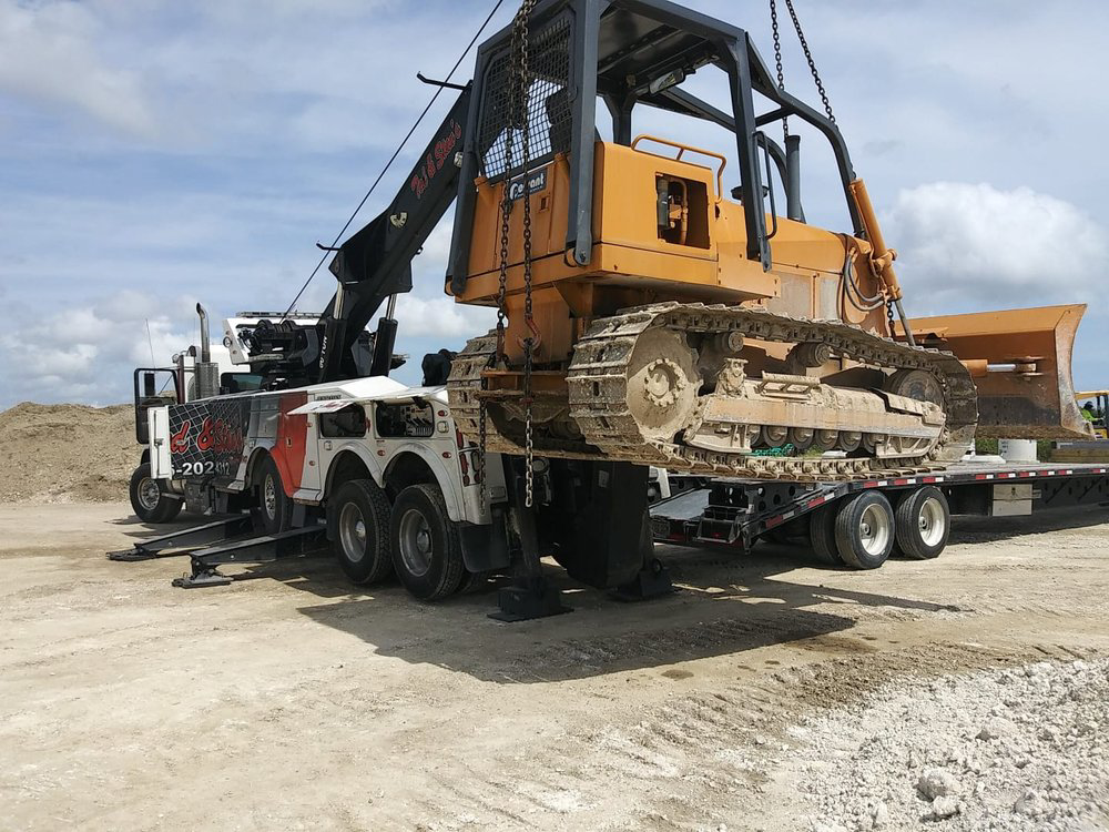 A heavy-duty tow truck from Ted & Stan's Towing Service lifting a bulldozer onto a flatbed trailer in Cutler Bay, FL.