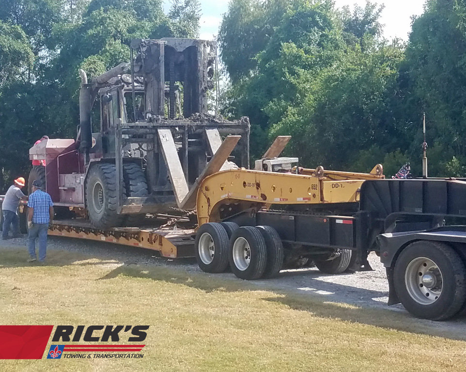 A heavy-duty truck from Rick's Towing and Recovery in Lafayette, LA, transporting burnt heavy machinery.