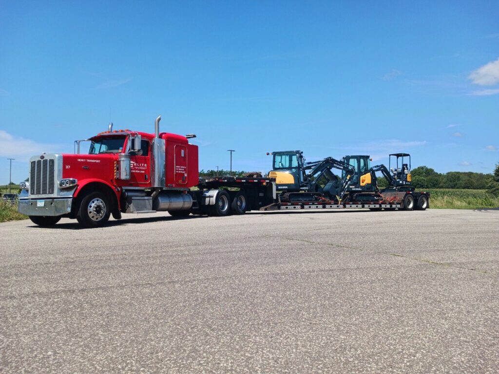 A red Elite Towing of Minnesota semi-truck transporting multiple excavators on a flatbed trailer in St Paul, MN.