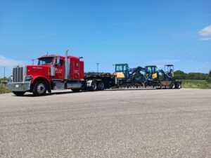 A red Elite Towing of Minnesota semi-truck transporting multiple excavators on a flatbed trailer in St Paul, MN.