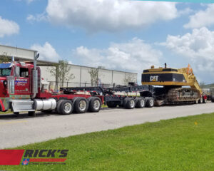 A heavy-duty truck from Rick's Towing and Recovery in Lafayette, LA, transporting a large yellow excavator.