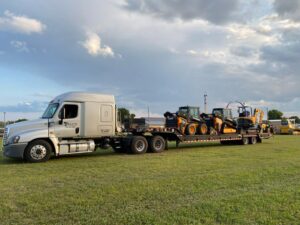A white Elite Towing of Minnesota semi-truck transporting multiple excavators on a flatbed trailer in St Paul, MN.