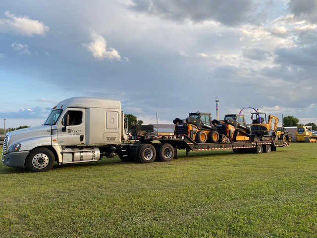 A white Elite Towing of Minnesota semi-truck transporting multiple excavators on a flatbed trailer in St Paul, MN.