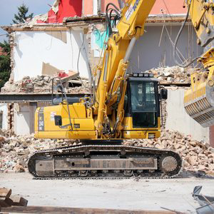 A large yellow excavator with a demolition attachment tearing down a building, representing DEMO Leaders in Los Angeles, CA