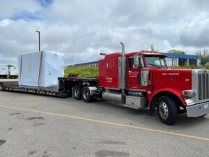 A red Elite Towing of Minnesota semi-truck transporting a large white wrapped object on a flatbed trailer in St Paul, MN.