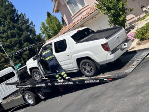 An AJ's Towing Services & Roadside Assistance operator loading a white Honda Ridgeline onto a flatbed tow truck in Sacramento, CA.