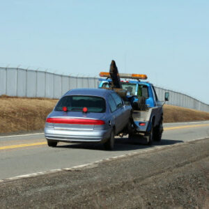 A hook-and-chain tow truck towing a blue car for AE Recovery and Towing in Phoenix, AZ.