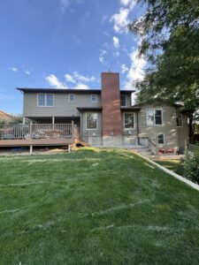 Rear view of a house with new gray siding and a brick chimney, installed by EZ General Construction in Colorado Springs, CO.
