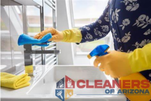 A house cleaner in yellow gloves meticulously cleaning a bathroom faucet with a spray bottle at Cleaners of Arizona in Chandler, AZ.
