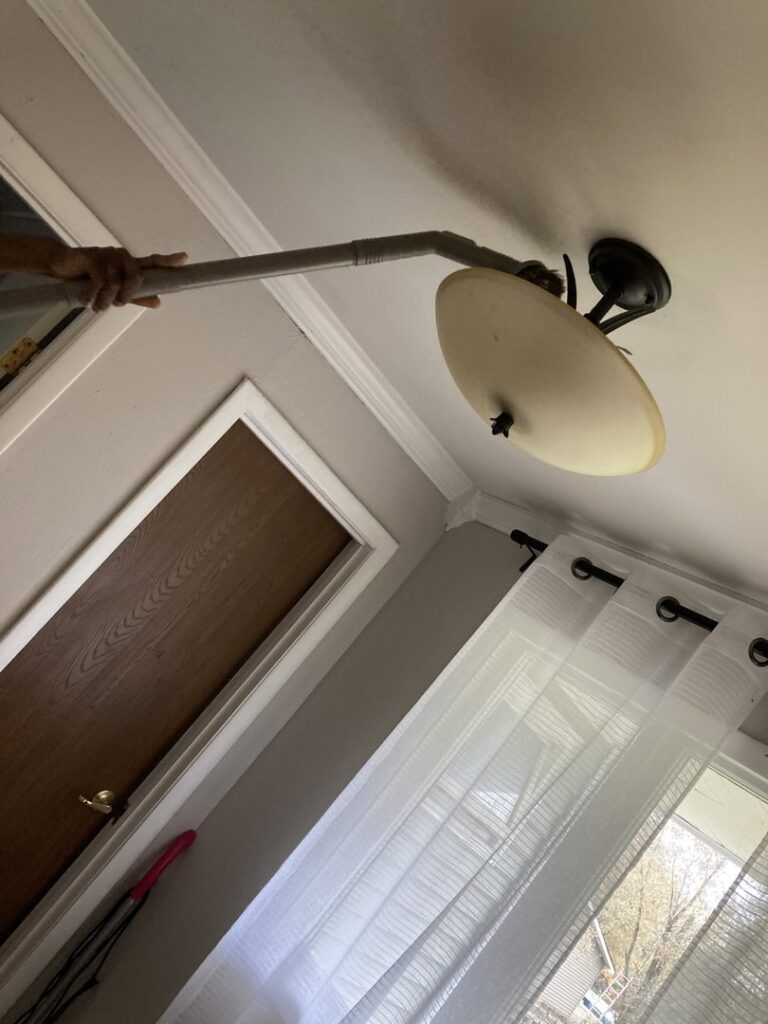 A house cleaner from G & S Cleaning Services cleaning a ceiling light fixture in Somerville, NJ.