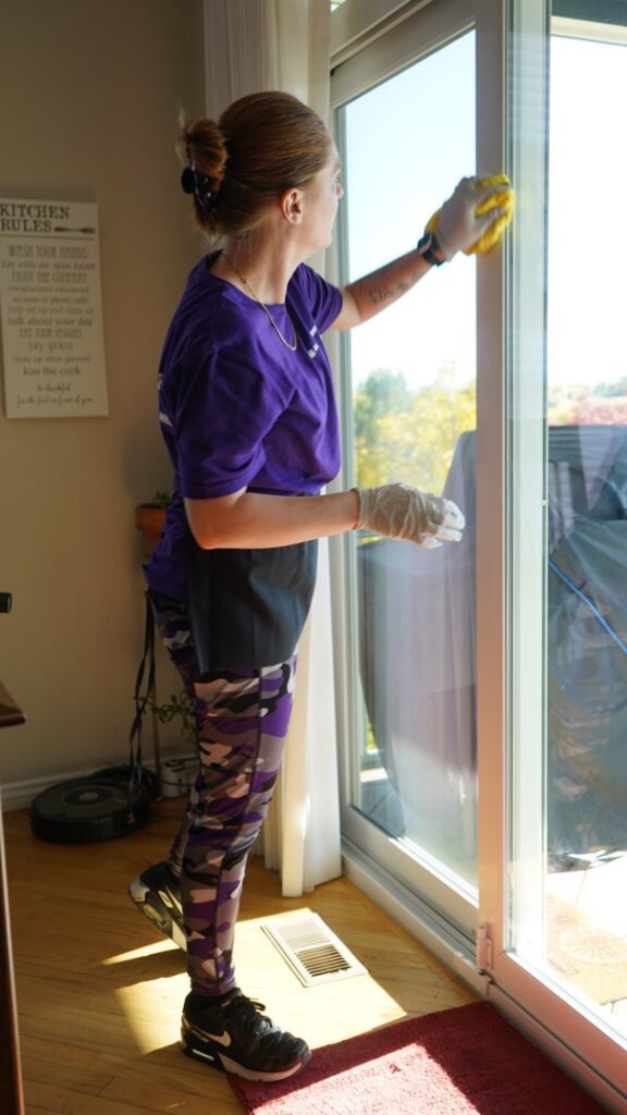 A house cleaner from Clean Queen House Cleaning cleaning a large glass sliding door in Arvada, CO.
