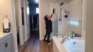 A professional house cleaner from ECO Friends cleaning service cleaning a glass shower door in a modern bathroom in Carson City, NV.