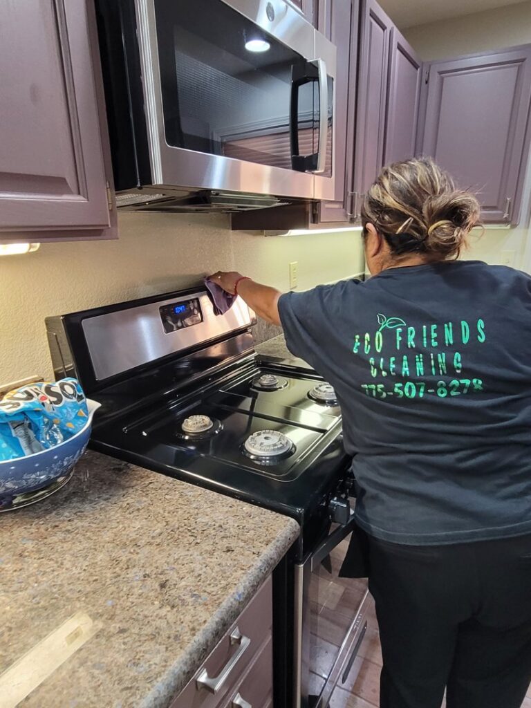 A professional house cleaner from ECO Friends cleaning service cleaning a kitchen stovetop and oven range in Carson City, NV.