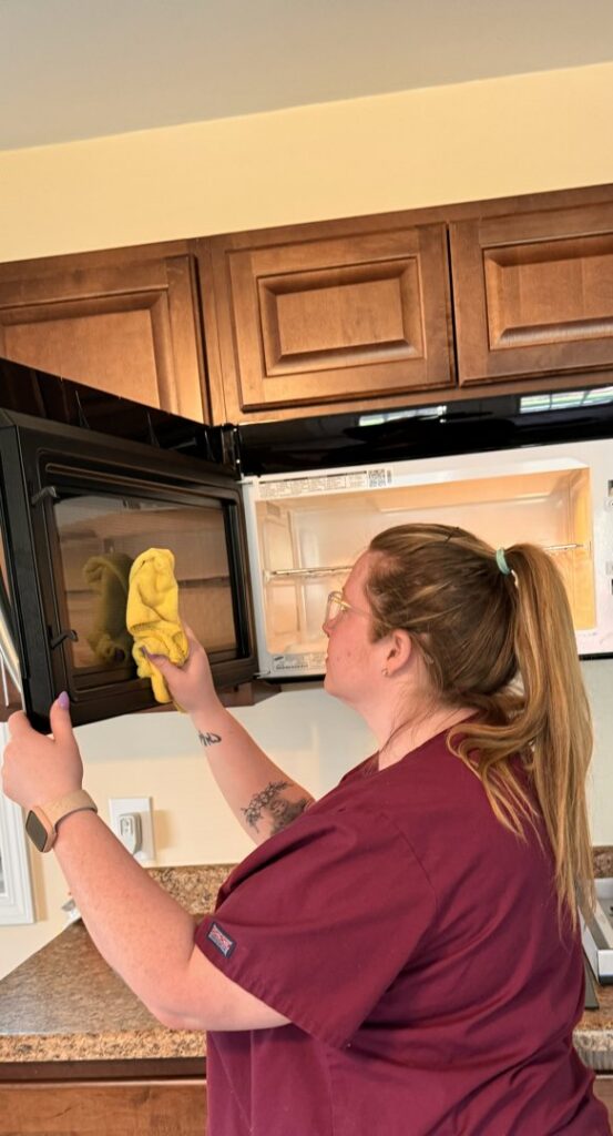 A house cleaner from Dirt Finders Maid Service cleaning the inside of a microwave in a kitchen in Evansville, IN.