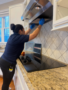 A house cleaner wearing blue gloves cleaning a range hood filter in a kitchen by Galvanhousekeeper LLC in Roanoke, VA