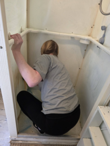 A house cleaner meticulously cleaning inside a shower stall for Clemons Cleaning service LLC in Jackson, MI.