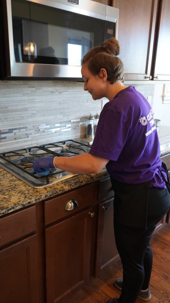 A house cleaner from Clean Queen House Cleaning cleaning a gas stovetop in a kitchen in Arvada, CO.