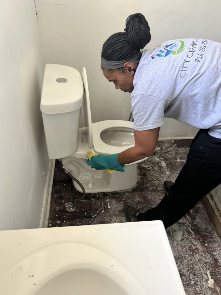 A house cleaner from City Cleaning Crew in Buffalo, NY, wearing gloves and cleaning a toilet.