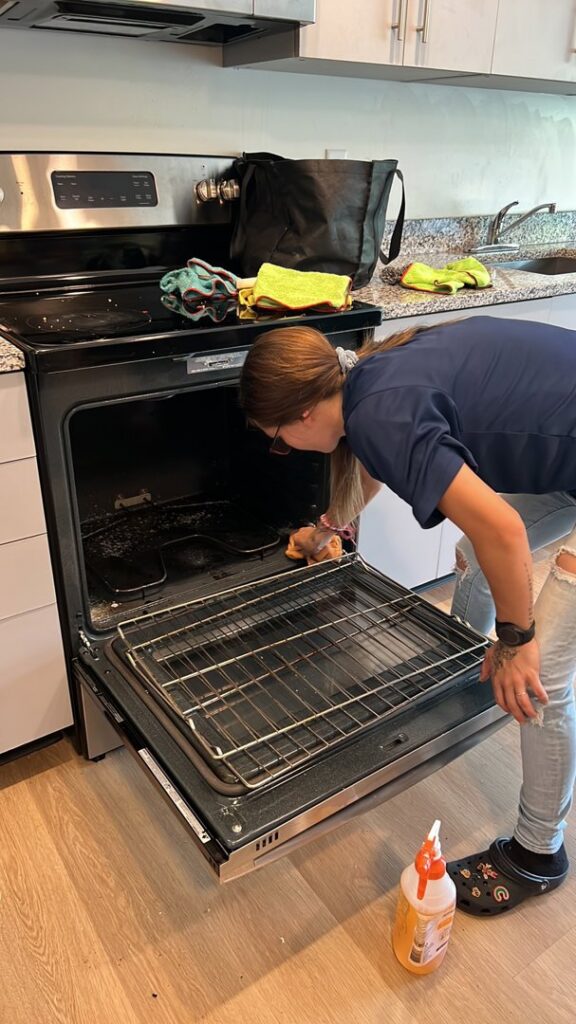 A house cleaner from City Cleaning Crew in Buffalo, NY, performing a deep cleaning of an oven interior.