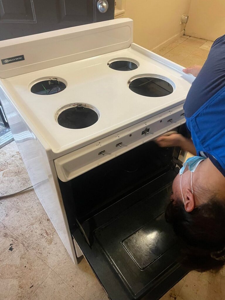 A house cleaner in a blue apron and mask meticulously deep cleaning the interior of an oven for Skedaddle Cleaning Services in Eufaula, AL.