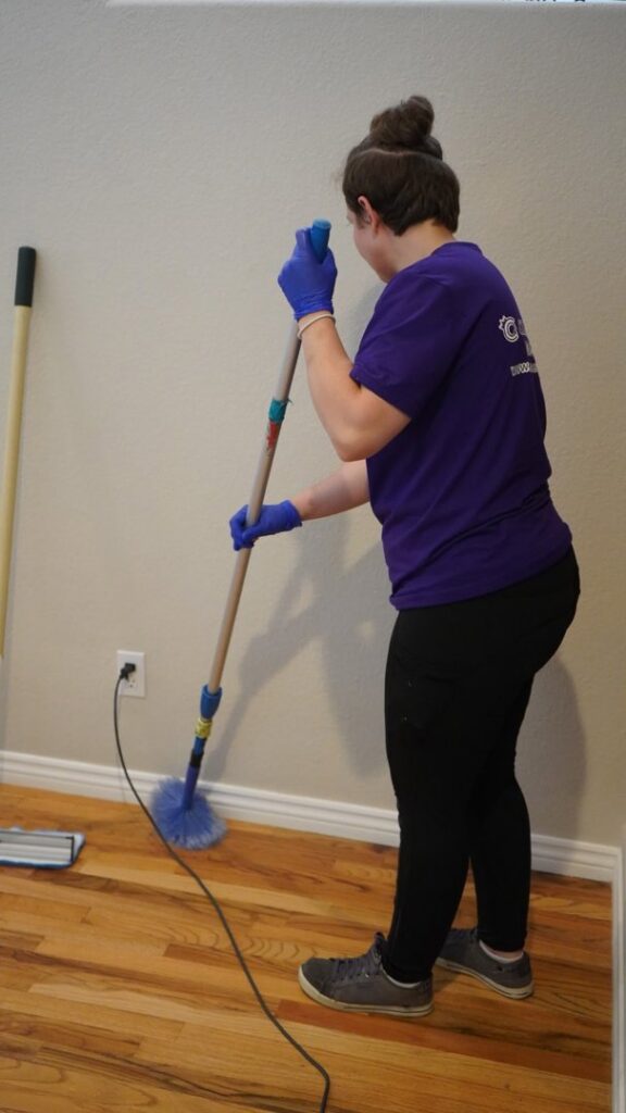 A house cleaner from Clean Queen House Cleaning dusting a baseboard with an extendable duster in Arvada, CO.